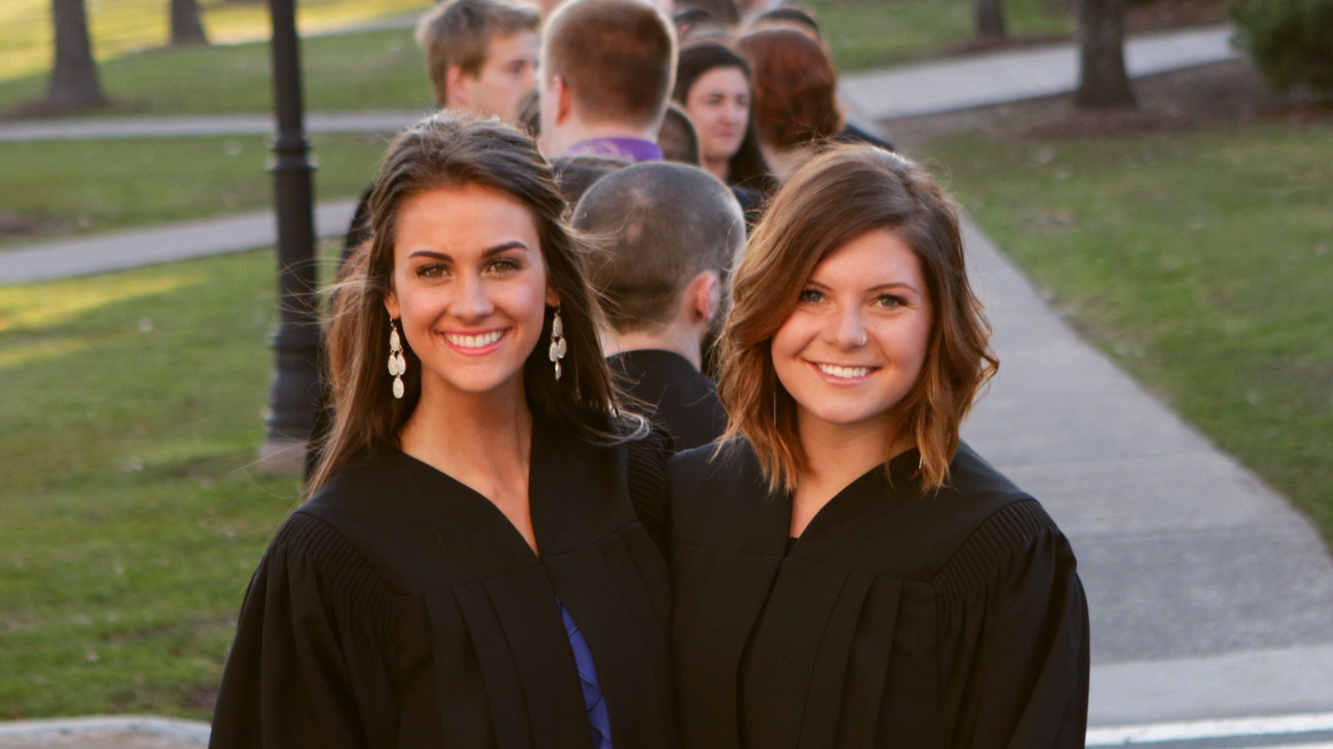 Close up of two students outside for the Xaverian Farewell ceremony. They are wearing their gowns and there are other students lined up behind them.