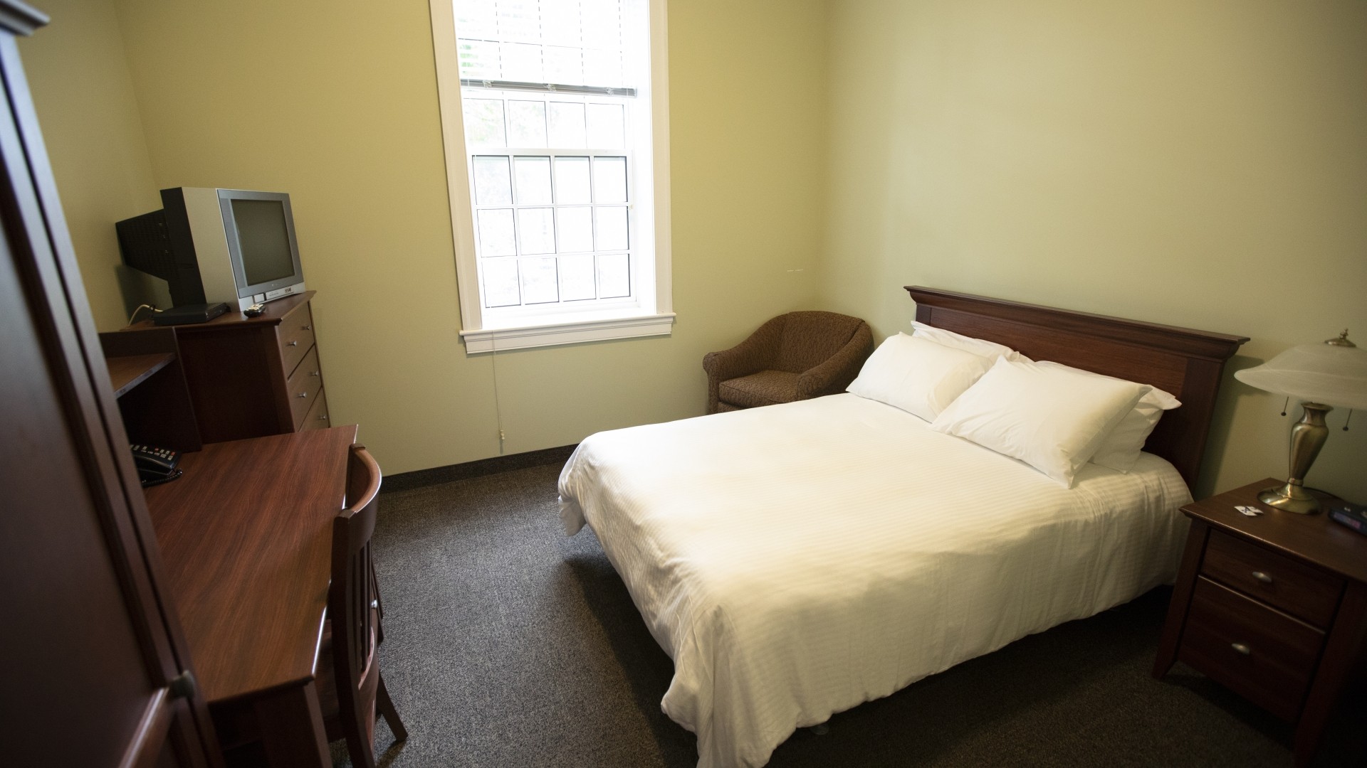 Single suite located in Governors Hall with a double bed, desk, TV, dresser and armchair.