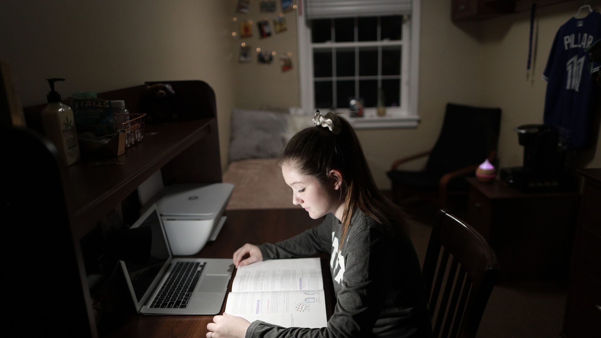 Student in their residence room studying while sitting at their desk on a dark evening.