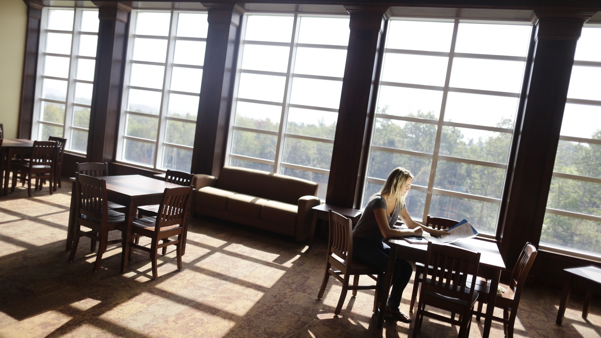 Student studying in a common lounge area in O'Regan Hall. There are big windows with the sun shinning through. 