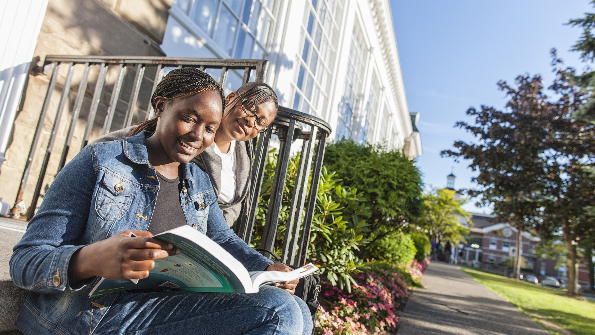Two students reading a book while sitting outside on Morrison Hall steps during a sunny day.