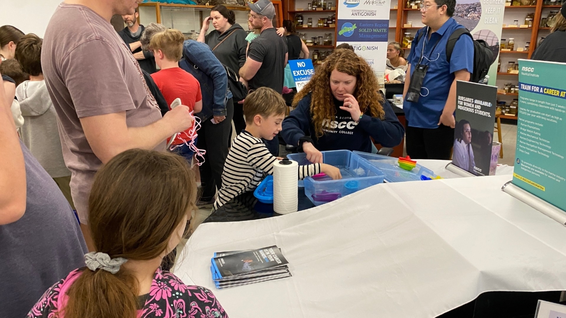 Children and adults participating in hands-on activities at an educational fair with informational tables and banners.