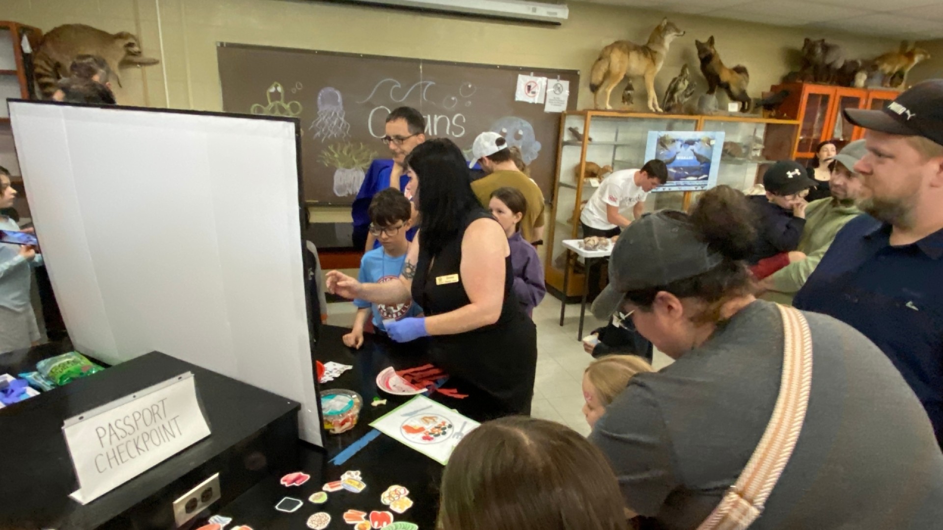 People gathered around a table labeled 'PASSPORT CHECKPOINT' with colorful cutouts, in an educational setting.