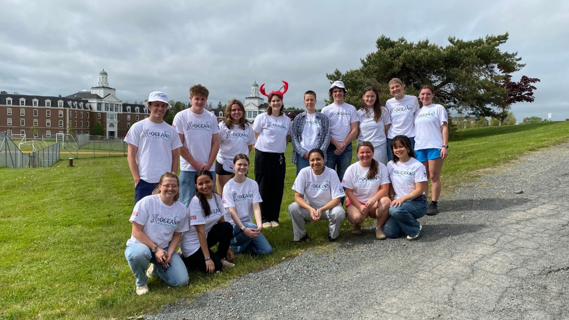 Group of people wearing 'SENIORS 2023' t-shirts posing outdoors on a grassy area with a building in the background.