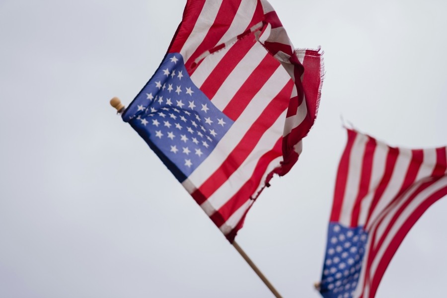 Two tattered US flags against a grey sky.