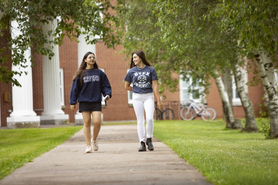 Students walking outside on a sunny day. There are trees around them and a bike rack in the background.