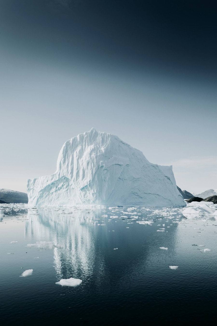 Large iceberg on water against a cloudy sky.