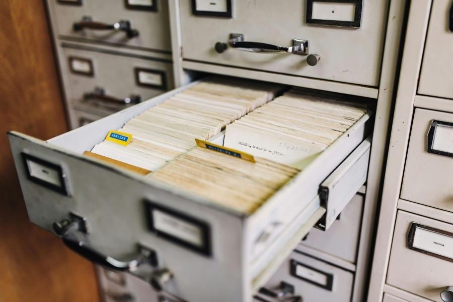 White filing cabinet with one drawer open and paper file cards inside.
