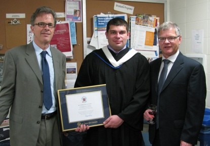 One graduated student showing his diploma, next to 2 men.