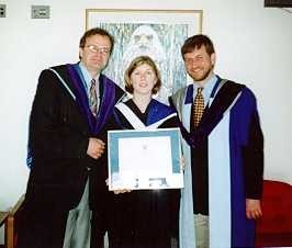 One graduated student showing his diploma, next to 2 men.