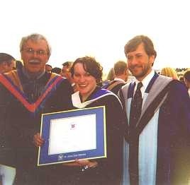 One graduated student showing his diploma, next to 2 men.
