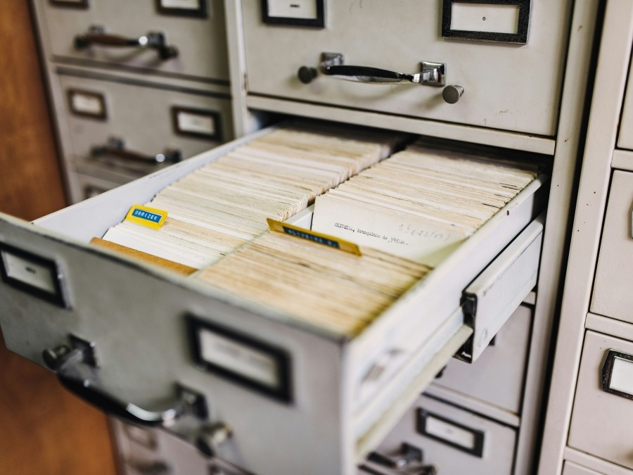 White filing cabinet with one drawer open and paper file cards inside.